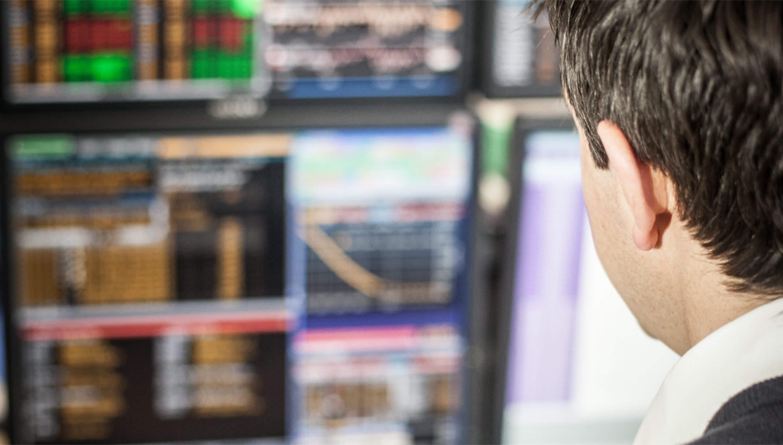 Close up behind a man looking at various computer screens showing data