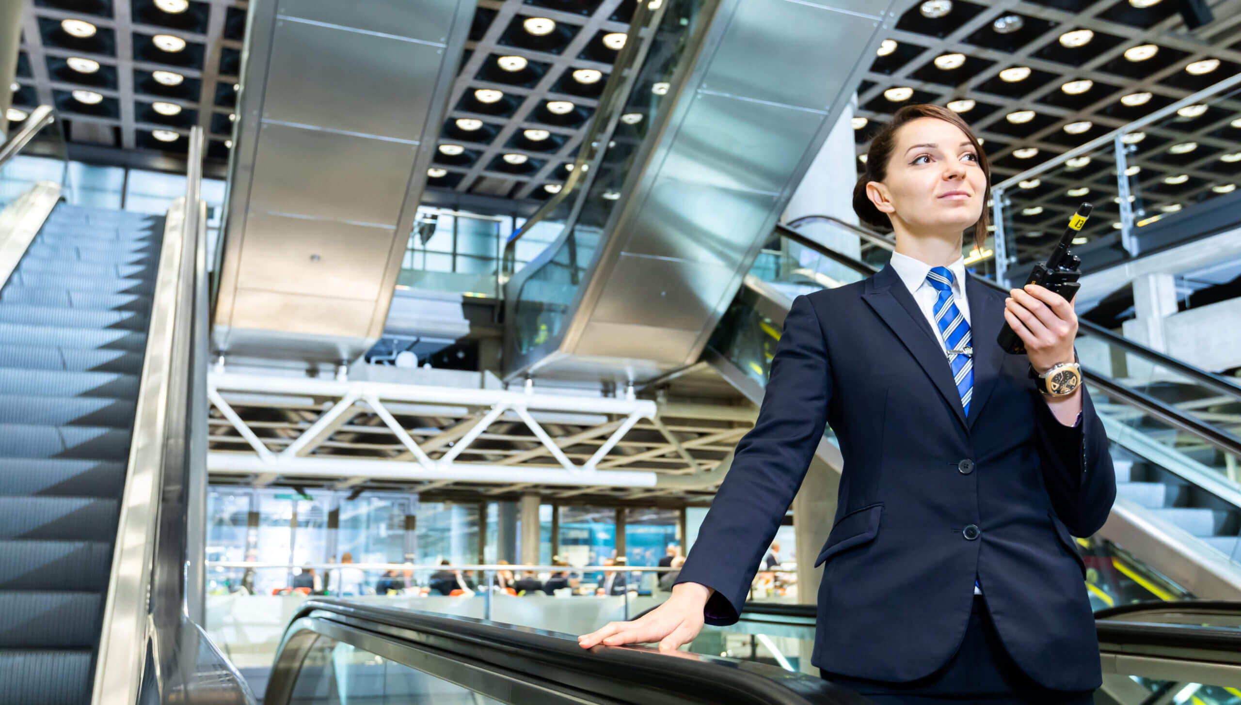 Female security officer using a radio in front of escalators