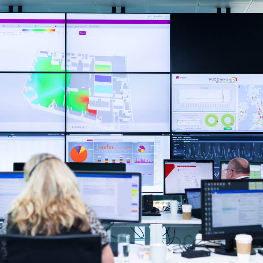 Several staff sitting at desks in front of a big screen showing data from a building