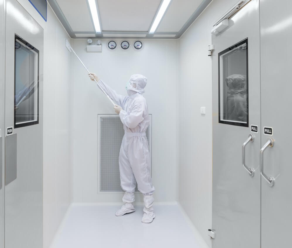 The inside of a sterile white room, with an employee dressed in white PPE cleaning one of the walls