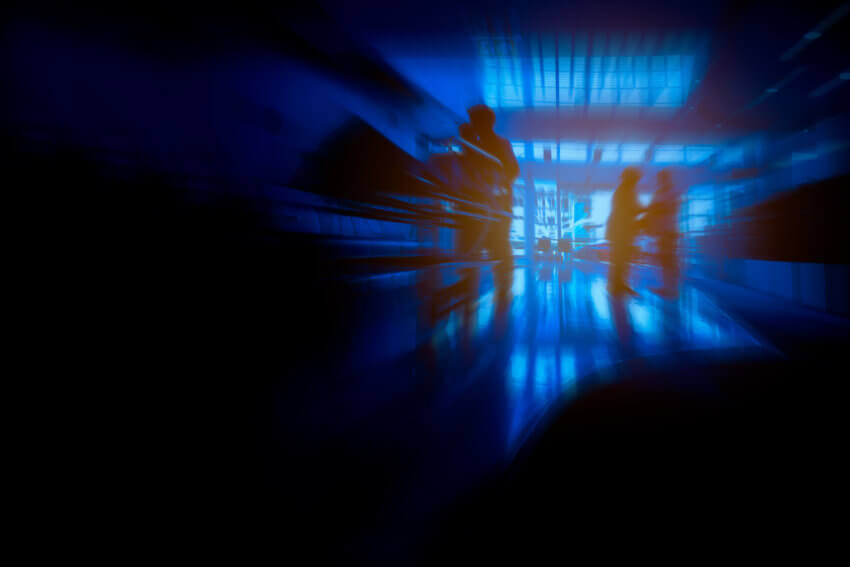 Dark blue and black image of silhouetted healthcare workers in a hospital reception