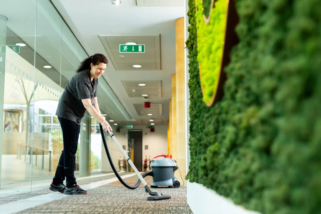 Woman hoovering an office near a green wall