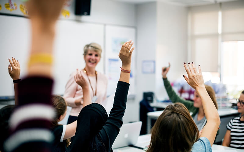 Students with their hands up responding to their teacher