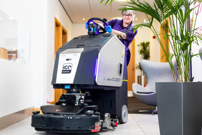 Mitie female cleaner turning the wheel on a robot floor cleaner in a corridor