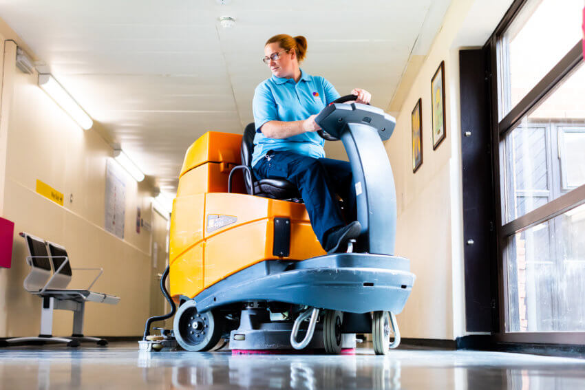 Women in a Mitie uniform sitting on and using a yellow floor cleaning machine