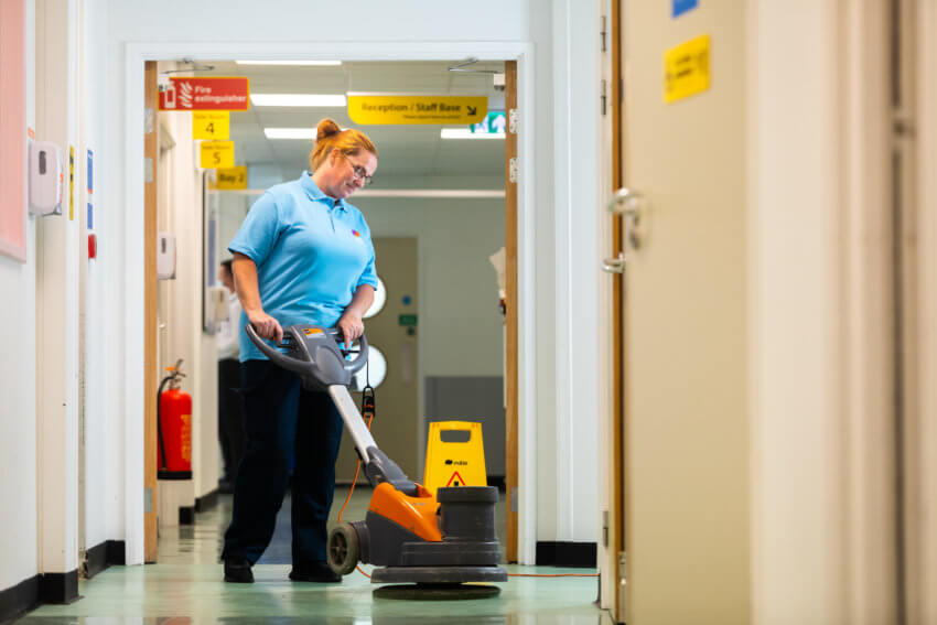 Mitie cleaning staff member using a floor polisher in a hospital corridor