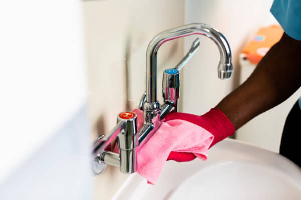 Chrome washbasin taps being cleaned with a pink cloth