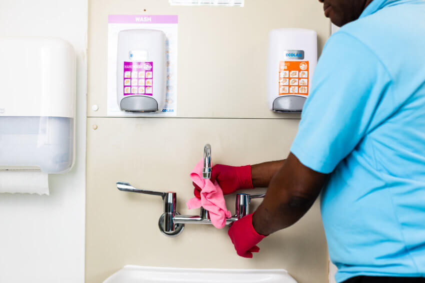Mitie employee cleaning a set of sink taps in a hospital with a pink cloth