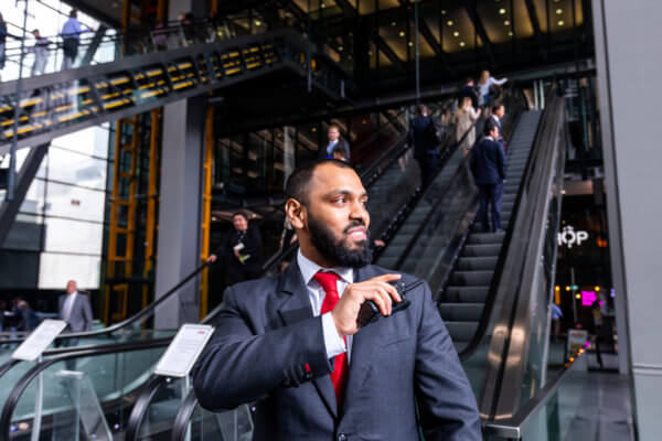 Mitie male security guard in a suit standing at the bottom of escalators