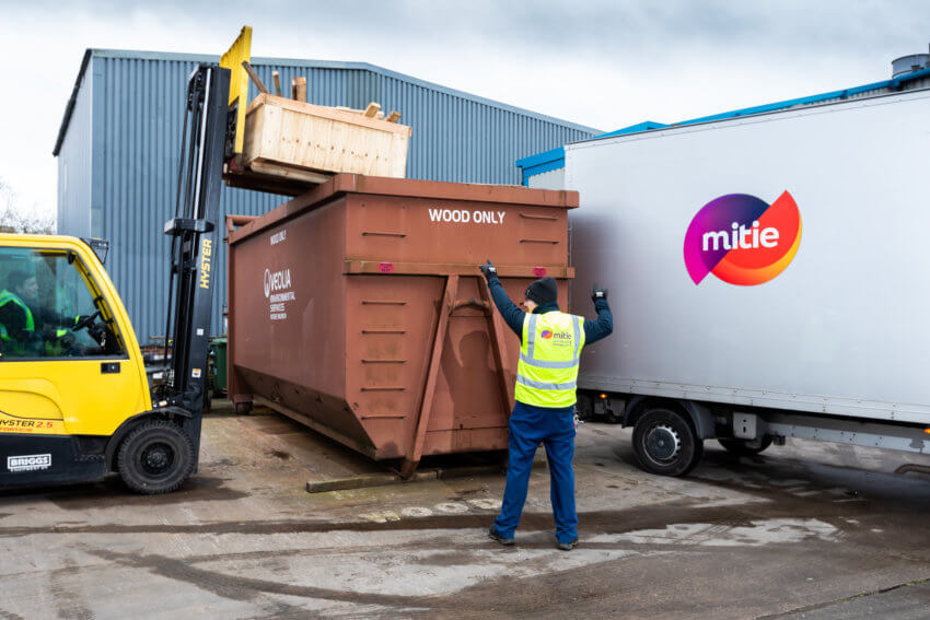 A man in a Mitie hi-vis vest directing wood to be disposed of in a large 'Wood Only' bin
