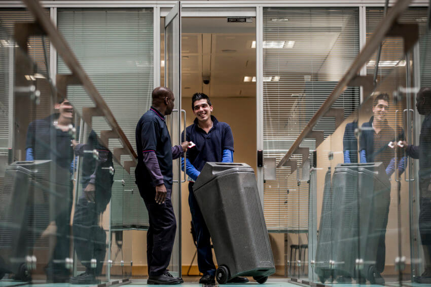 Two Mitie waste workers taking a grey bin out