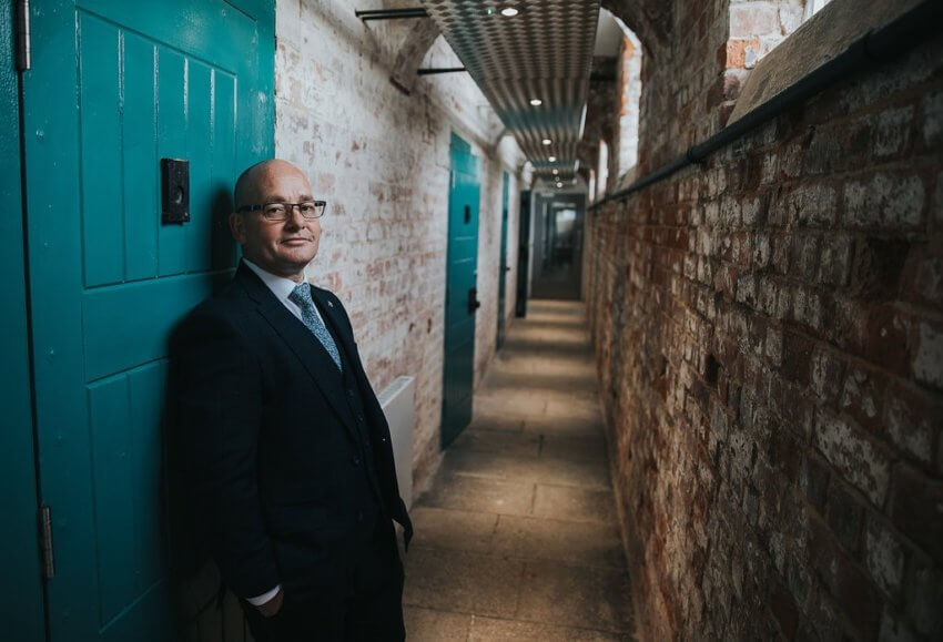 Gethin Jones, founder of Unlocking Potential, wearing a black suit in a prison corridor