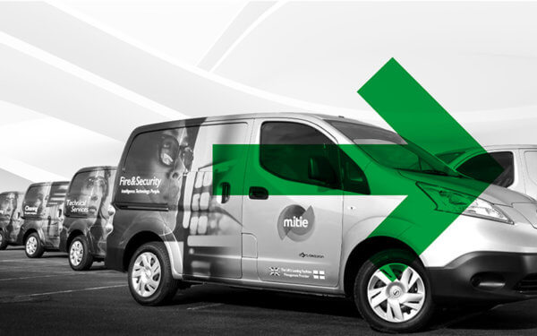 A line of Mitie vans in black and white, with a green arrow overlaid