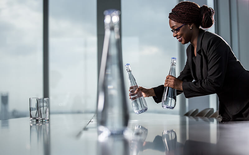 Woman placing glass water bottles on an office meeting table