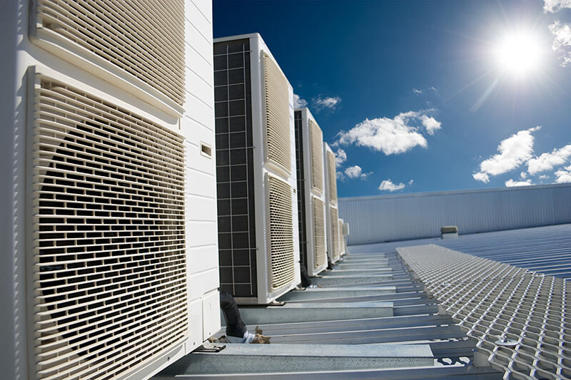 White air conditioner units on a roof of industrial building with blue sky and clouds in the background