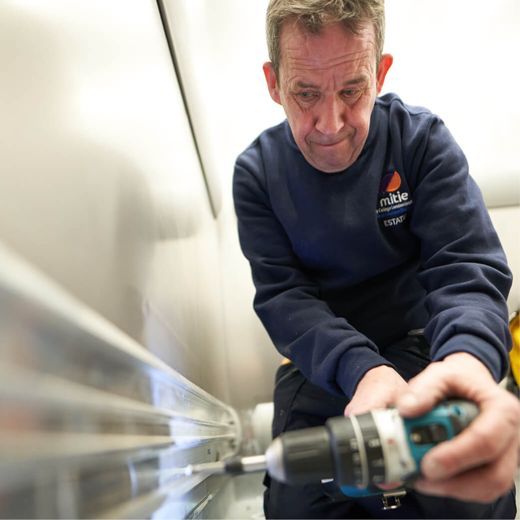 Mitie engineer using a drill and completing maintenance