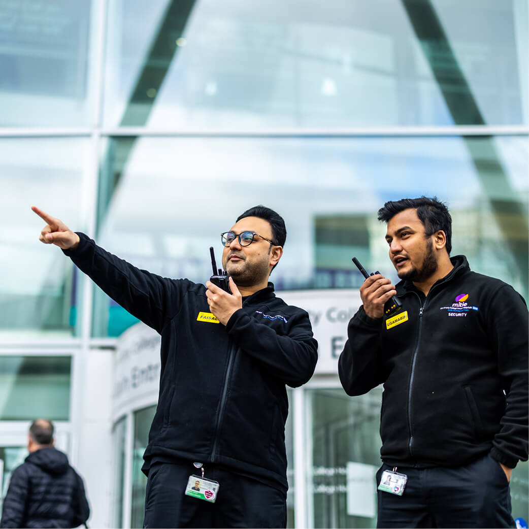 Two Mitie security guards standing and using walkie talkies outside a hospital