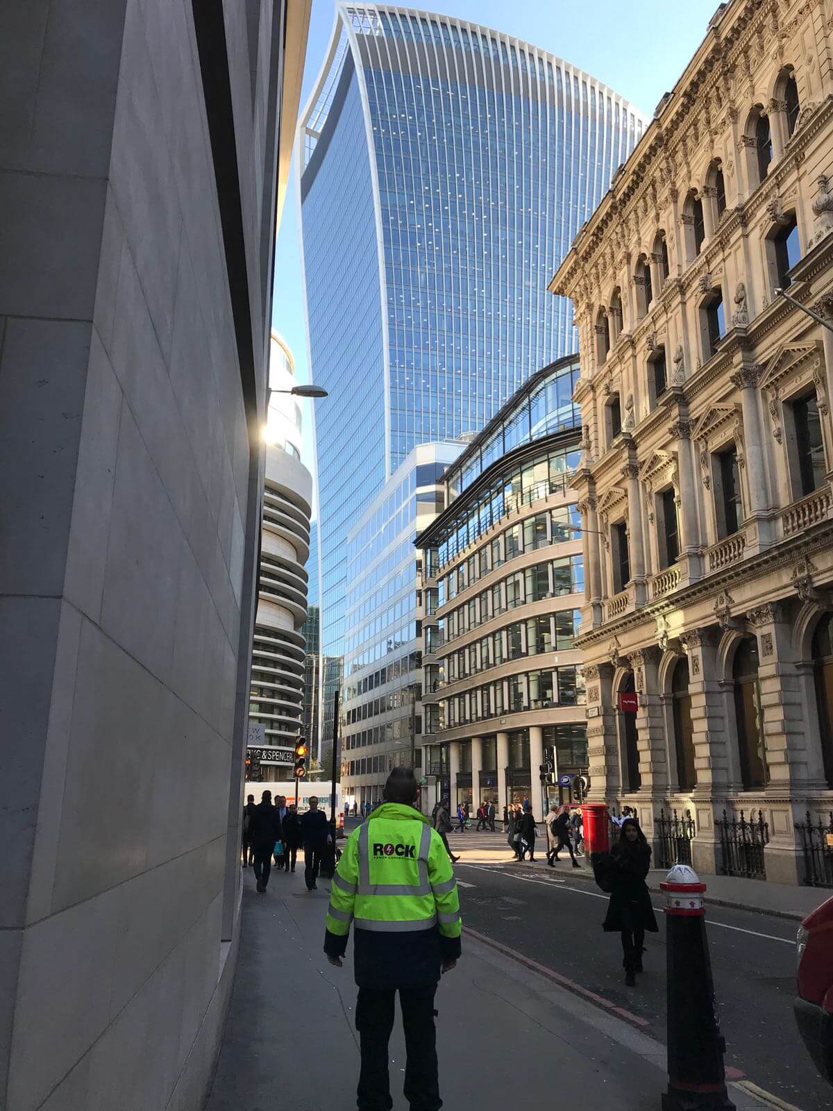 A Rock Power Connections employee in a hi vis jacket, looking up at a London skyscraper building