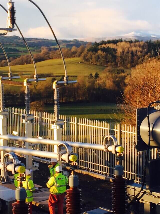 Rock Power Connection employees in high vis clothing, working on an electrical connection with the British countryside in the background