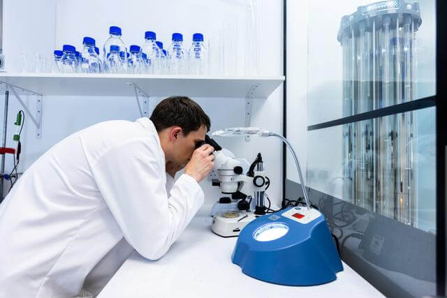 Lab assistant in a white lab coat looking in a microscope
