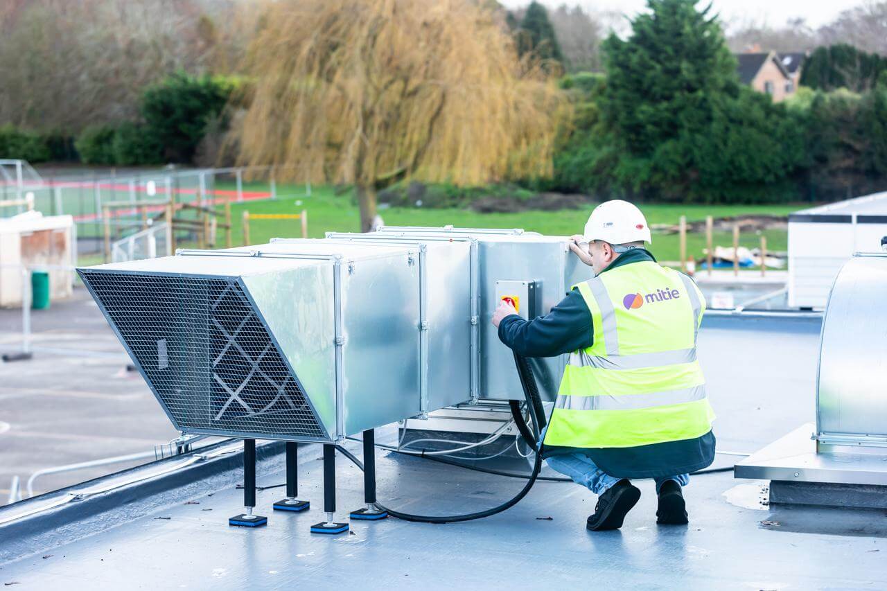 Mitie engineer in high-vis and hard hat working on a rooftop ventilation system