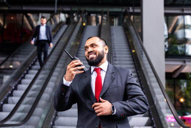 Security guard using a radio, standing at the bottom of escalators