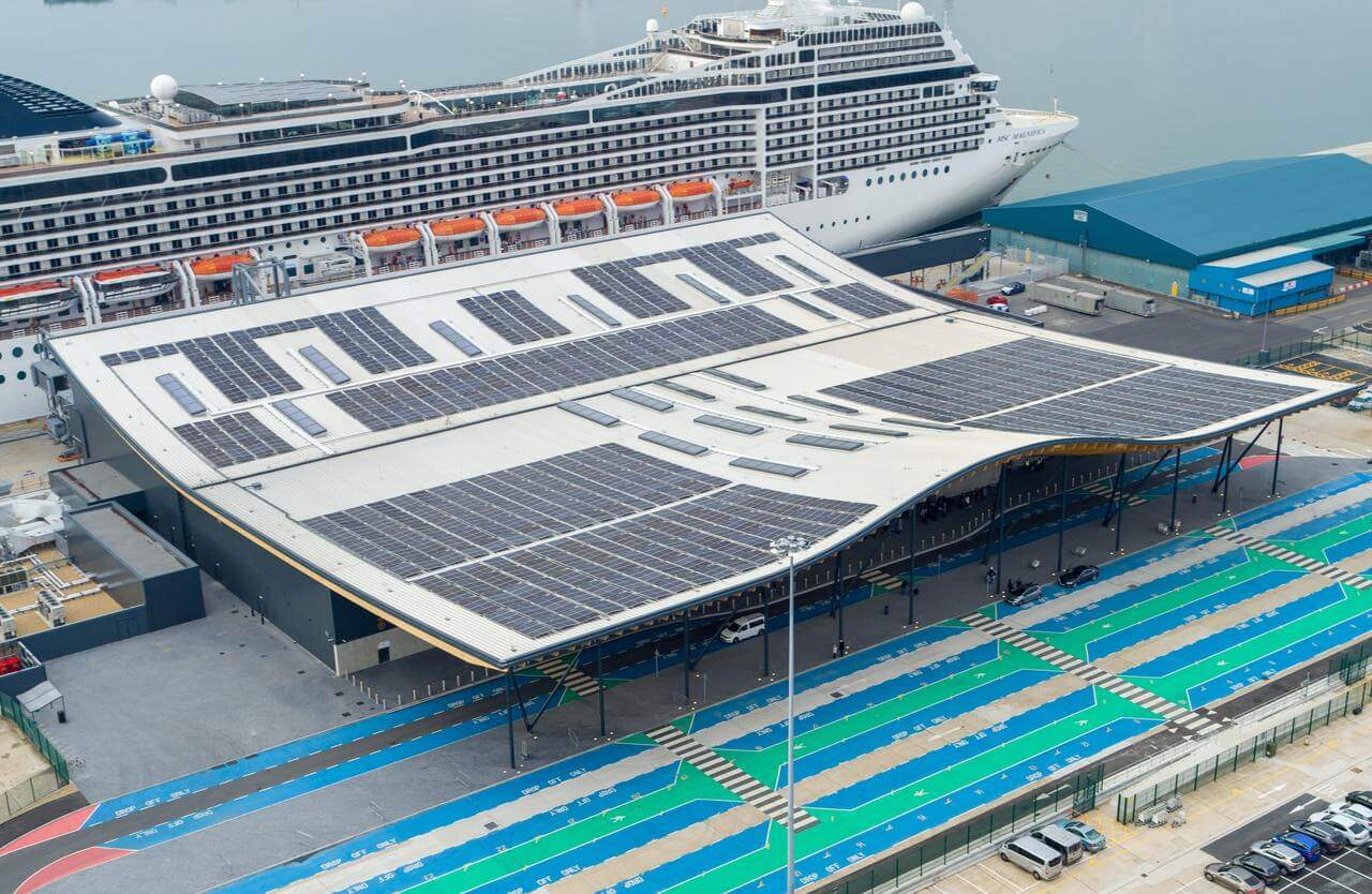 Solar panels on the roof of a cruise port terminal, with a cruise ship docked