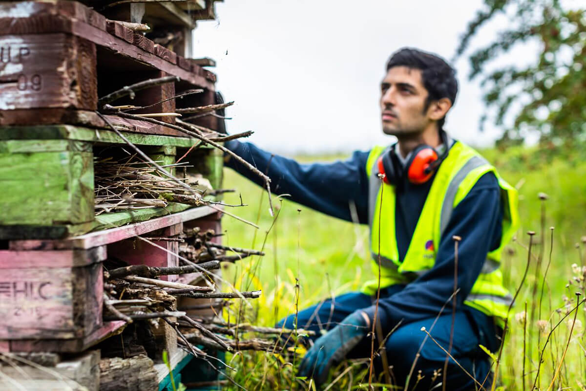 Mitie employee in high vis kneeling by a pile of old wooden pallets and sticks, created for wildlife
