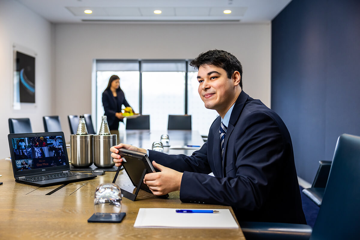 Male front of house employee sitting at a meeting table and helping to set up the technology