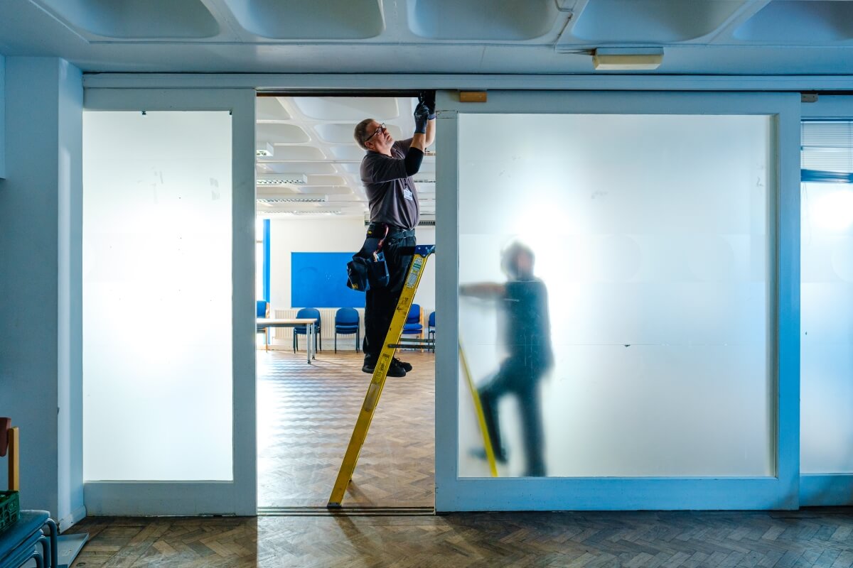 Mitie maintenance engineer up a ladder fixing a door at Sussex University