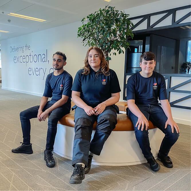 Three apprentices in Mitie t-shirts sitting in an office environment