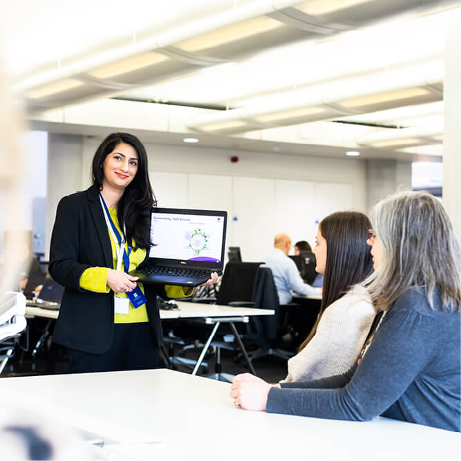 Professional woman in an office environment, showing a presentation slide on a laptop screen to colleagues