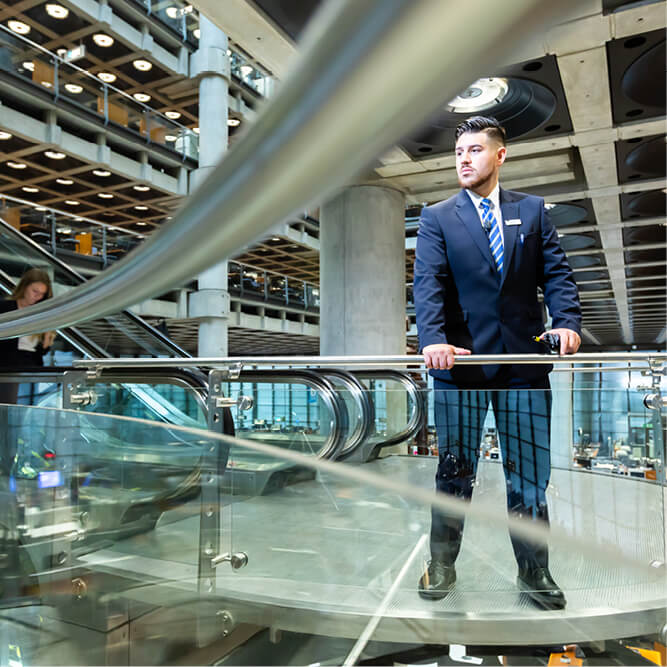 A male security guard in a suit looking over a rail in an office environment