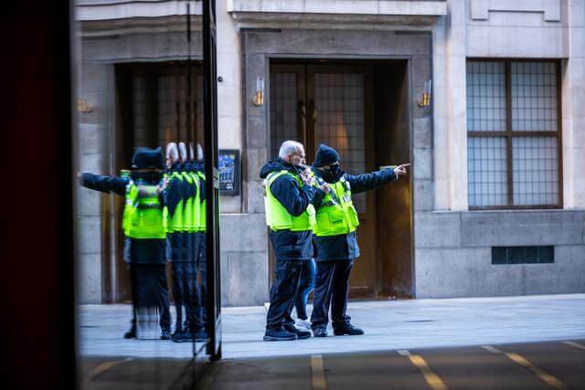 Two security guards in high vis pointing down a London street
