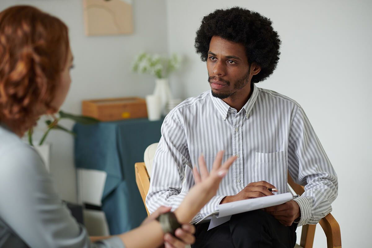 Man taking notes on a paper pad while talking to a woman