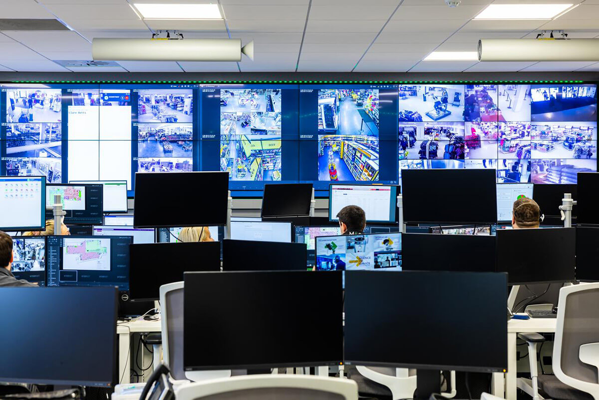 Various people working at desks with a wall of computer screens in front of them, showing a range of CCTV imagery