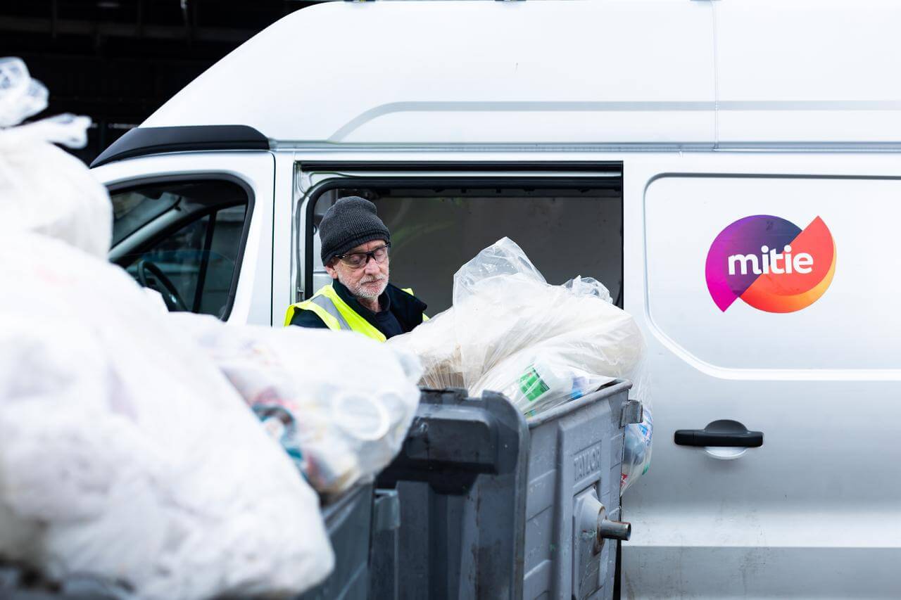 Mitie employee removing waste in plastic bags from roller bins, next to a van with the Mitie logo on the side