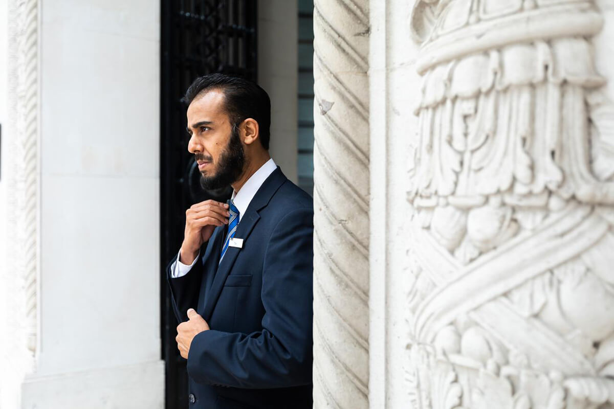 Security guard wearing a dark suit standing in a white marble doorway