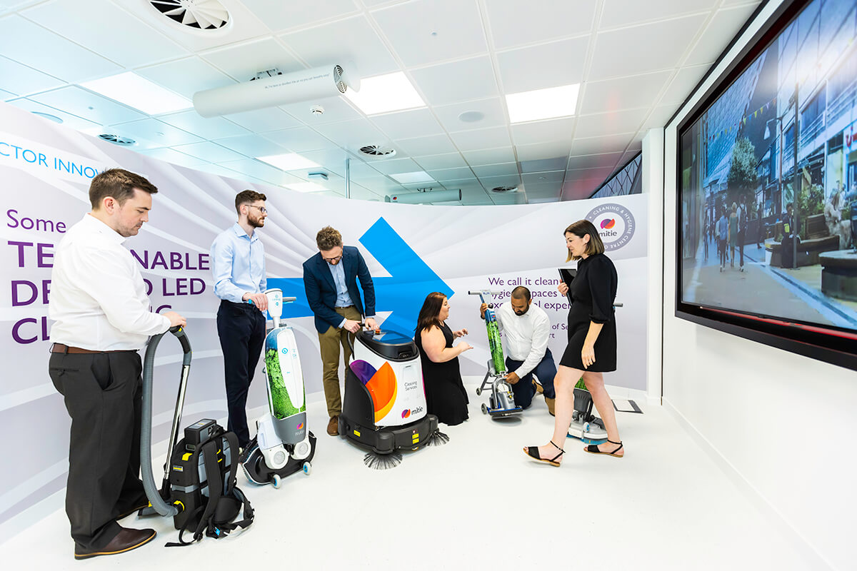 Various people trying out different cleaning robots and technology at the Mitie Cleaning and Hygiene Centre of Excellence