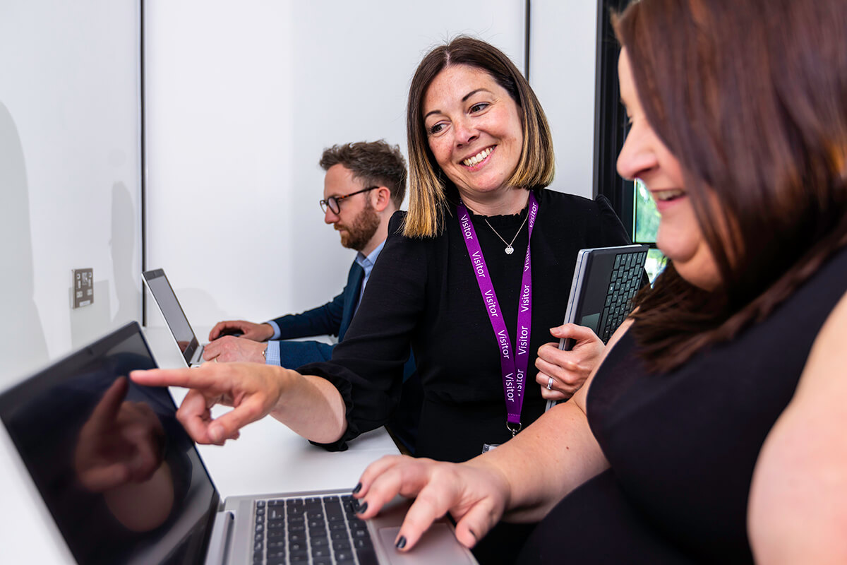 A woman pointing at a laptop screen and smiling in the learning zone of the Mitie Cleaning and Hygiene Centre of Excellence