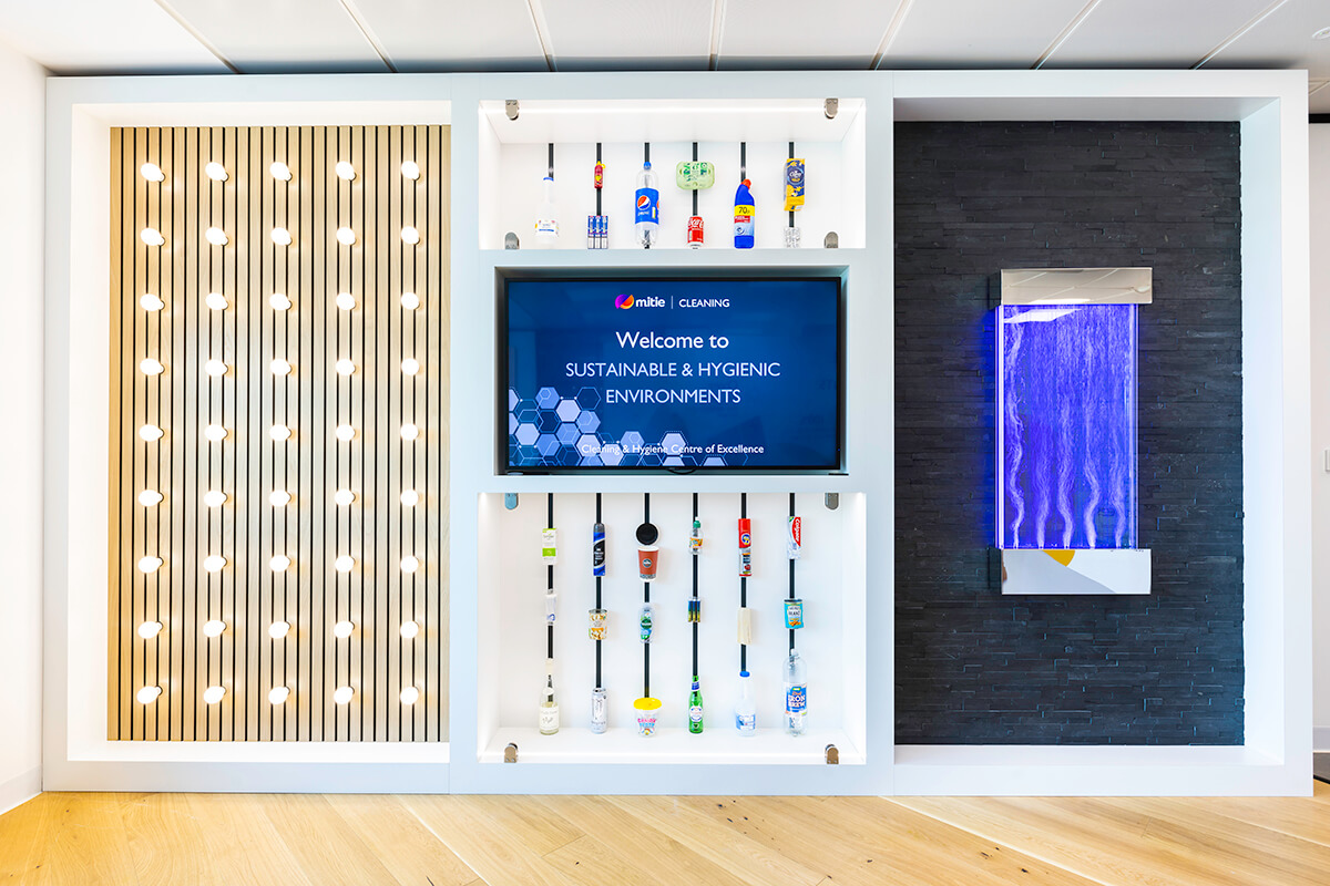 A wall displaying various empty containers for household products, lights, water jets and a flat-screen TV. Part of the Mitie Cleaning and Hygiene Centre of Excellence