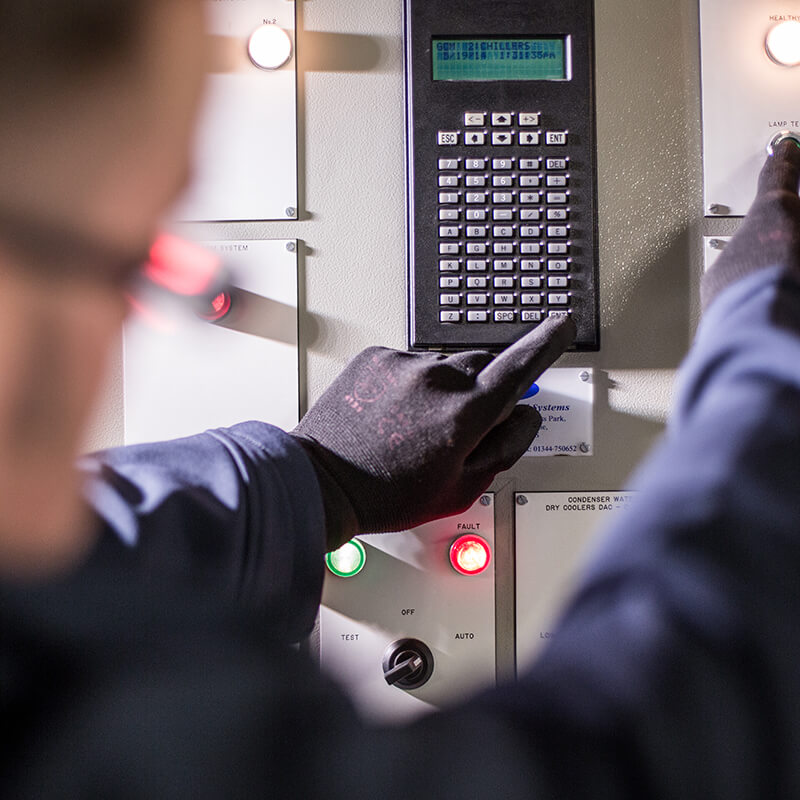 Close up of a Mitie engineer wearing black gloves pressing buttons on a control panel