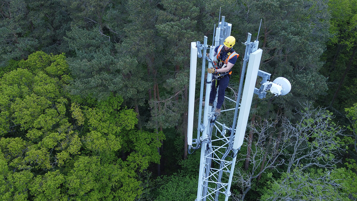 Mitie employee at the top of a telecoms mast, with green treetops below