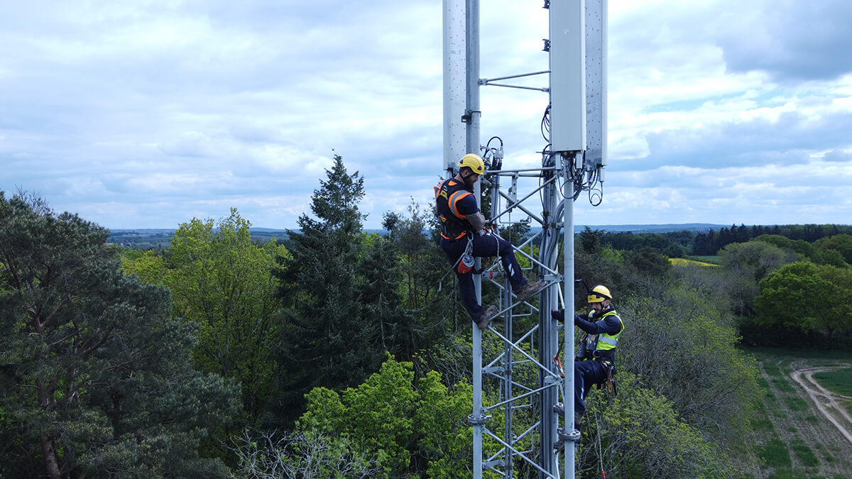 Two Mitie employees at the top of a telecoms tower, with green trees and fields in the background