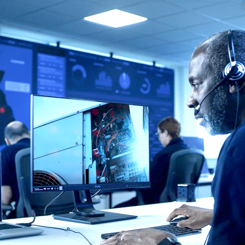 A remote maintenance worker at Mitie's Technical Services Operations Centre. Wearing a headset and looking at a monitor, seeing what an engineer is seeing on site