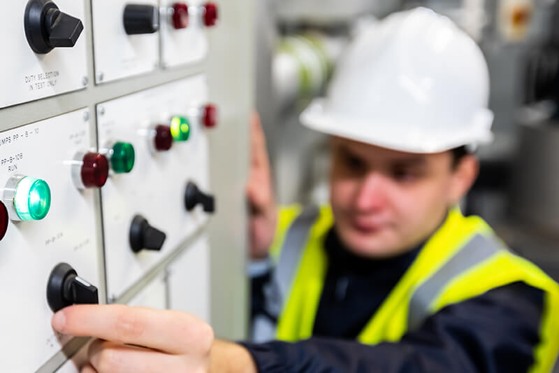 Engineer in high-vis vest and hard hat twists a dial on a large machine