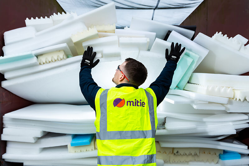 A Mitie employee, wearing a branded high-vis vest, pushing a large amount of foam and polystyrene waste