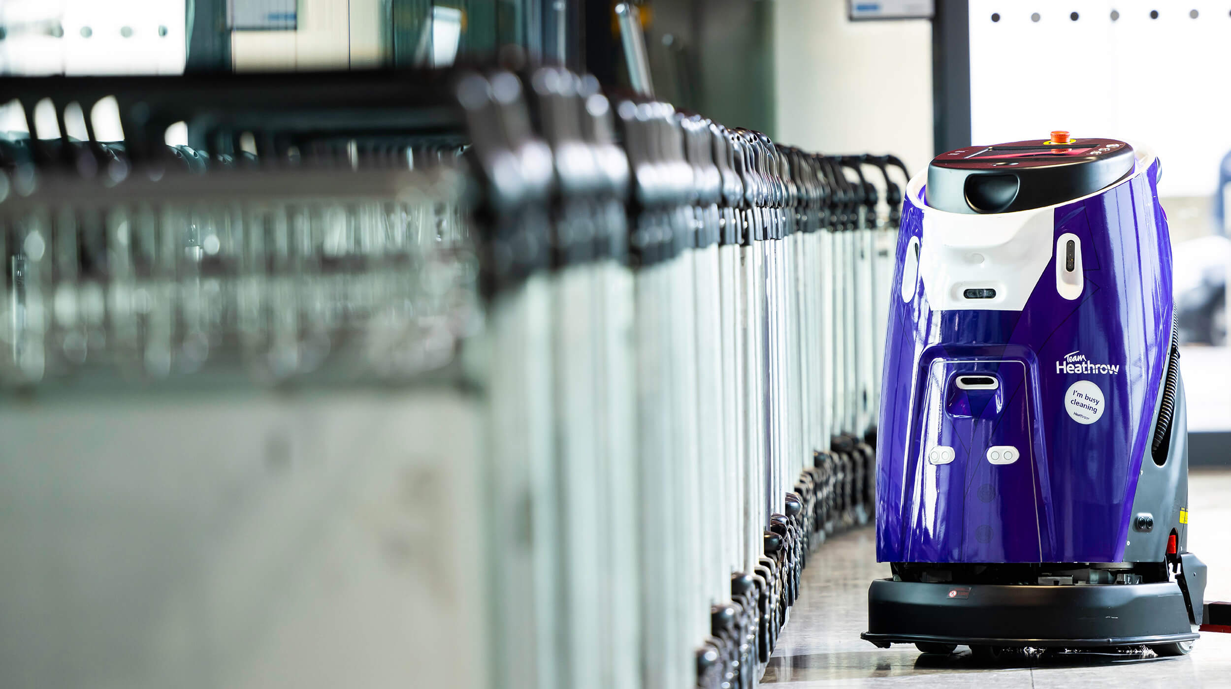 Mitie cleaning robot at London Heathrow Airport, next to a line of baggage trolleys