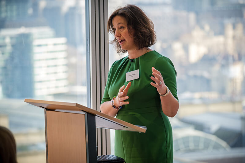 Catherine Wheatley, Mitie's Head of Data and Technology, presenting at Mitie's Carbon Disclosure event - standing in front of a wooden lectern by a window in The Shard, London