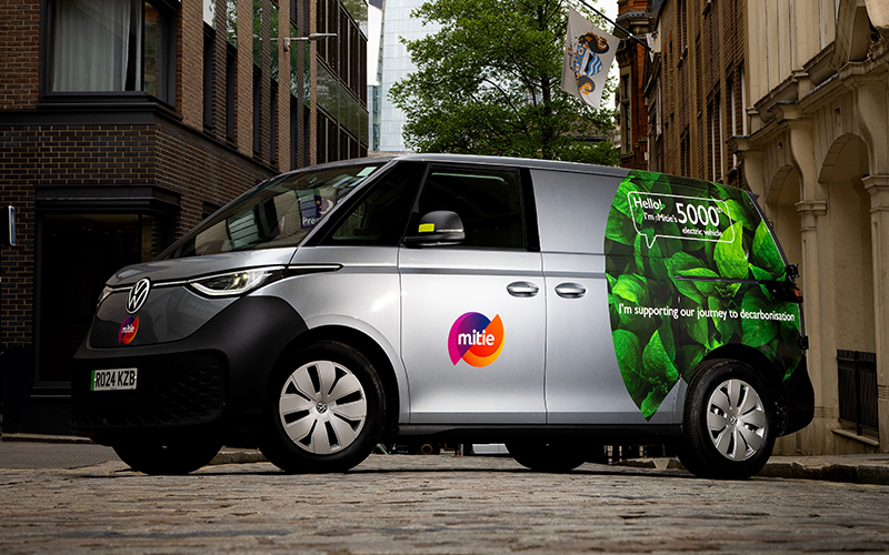 Mitie branded electric van - grey van with green leaves on the rear, with text of 'Hello! I'm Mitie's 5000th electric vehicle'